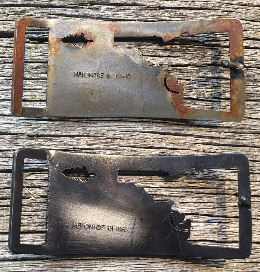 Idaho Tree-Gun Steel belt buckle, Idaho shooting a pine tree, Rust finish, Gunmetal finish, and Raw Steel finish